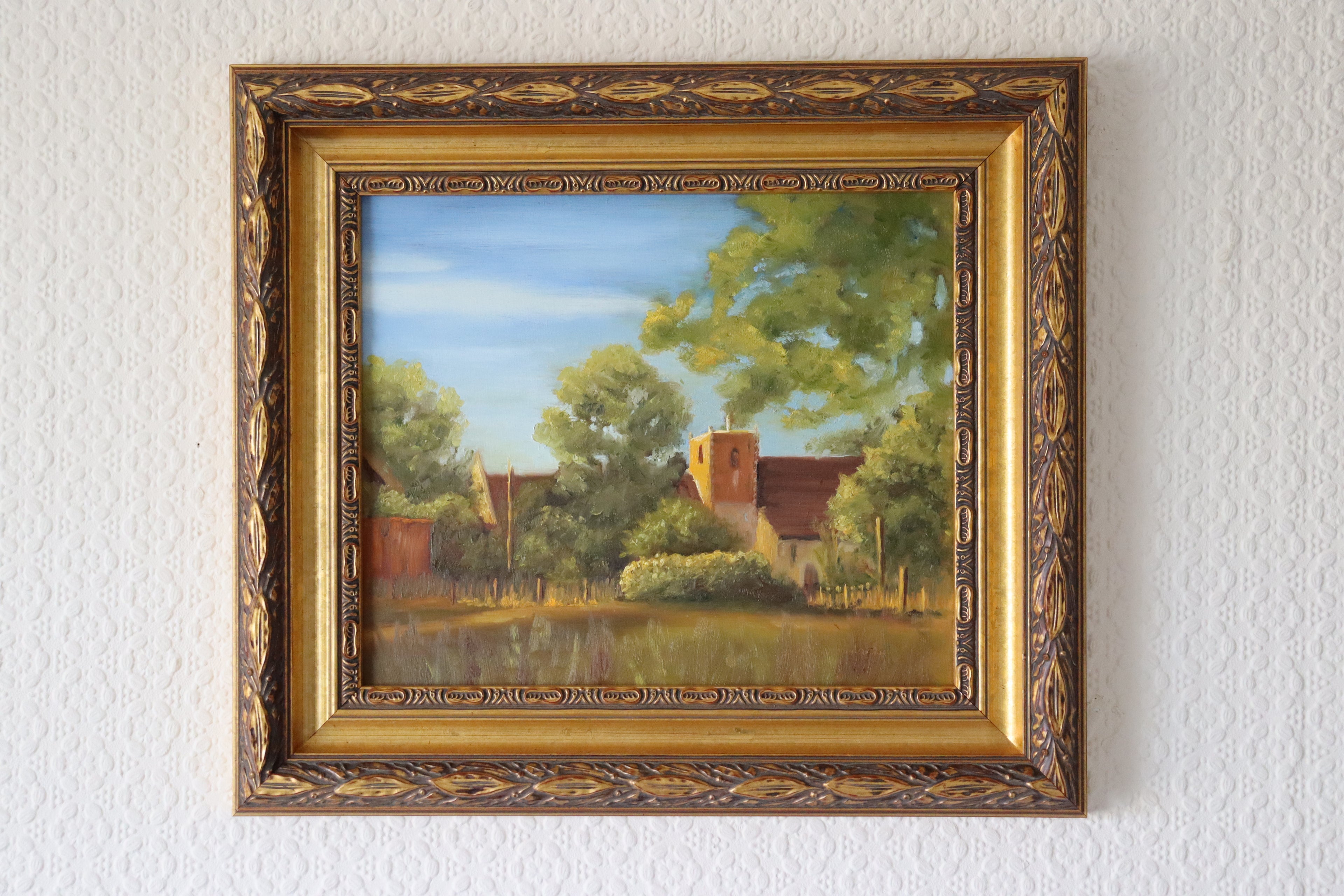 Framed original oil painting of St Michael's Church Oulton Broad in golden sunset light.Framed painting of a landscape with trees and a building on a white wall.