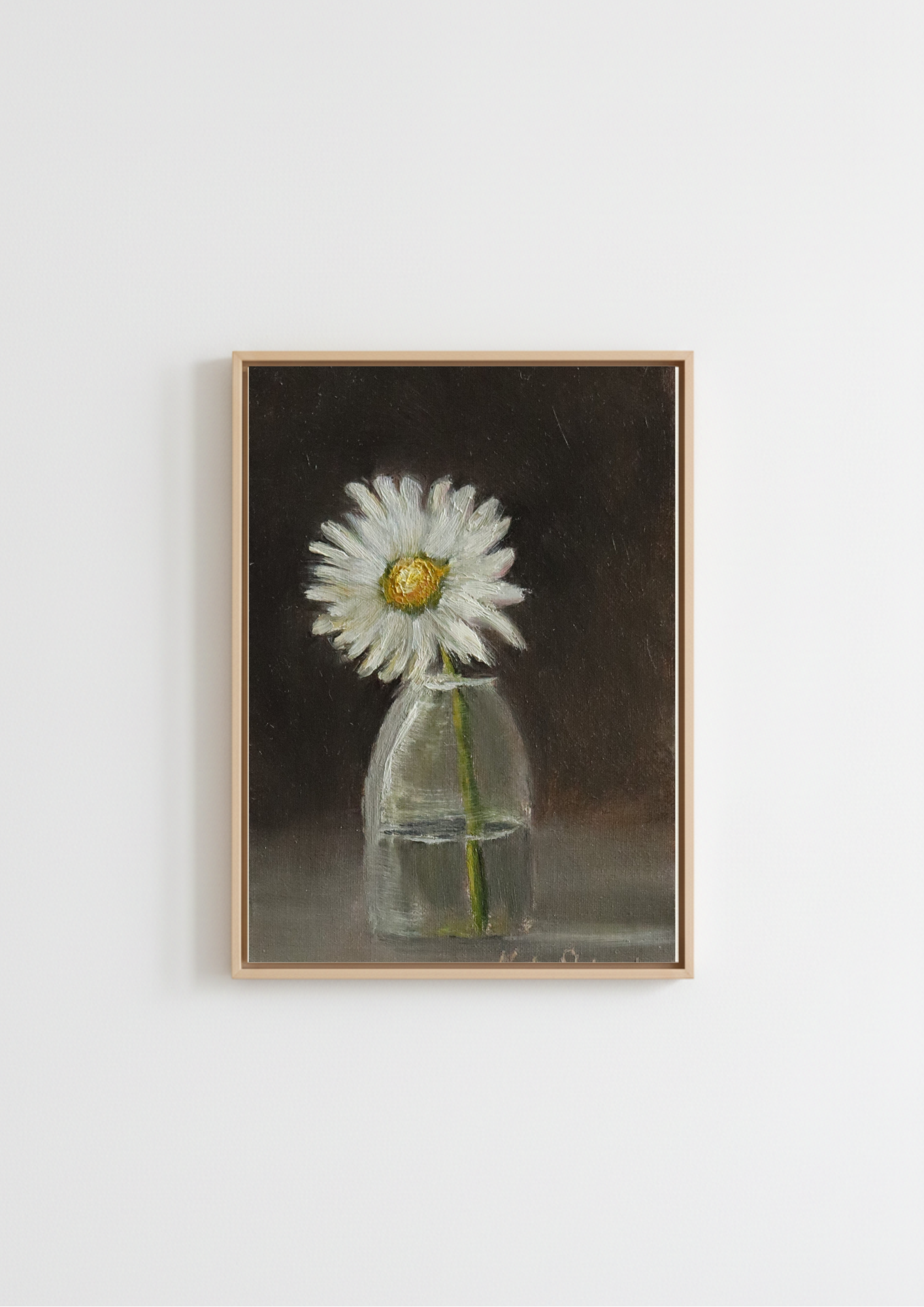 A framed still life painting of a white daisy in a clear glass vase against a dark brown background, hung on a plain white wall. The Garden Daisy - original oil painting by Marta Stolarska, a single white daisy in a small glass vase against a dark background, painted from life on handmade linen board, 10 x 15 cm