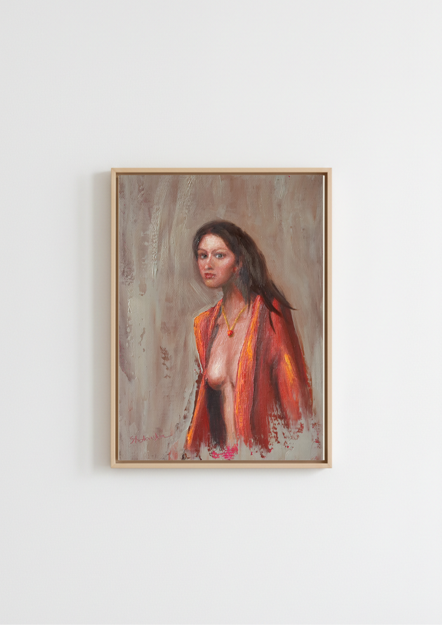 A framed portrait painting of a woman with dark hair, wearing a bright orange-red shawl, hanging on a plain white wall. The Interrupted Moment - original oil figure painting by Marta Stolarska, dark-haired woman in slightly open red robe turning to look back at viewer, oil on canvas board, gold frame 25.5x30.5cm