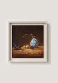 A framed still life painting featuring a blue and white patterned vase, grapes, and small fruits on a warm brown tabletop against a dark background, displayed in a light wood frame on a neutral wall. The Warmth of the Autumnal Glow - original oil painting by Marta Stolarska, oranges, grapes and leaves in a white and blue vase, autumnal light glowing across the composition, 20x20cm deep edge canvas