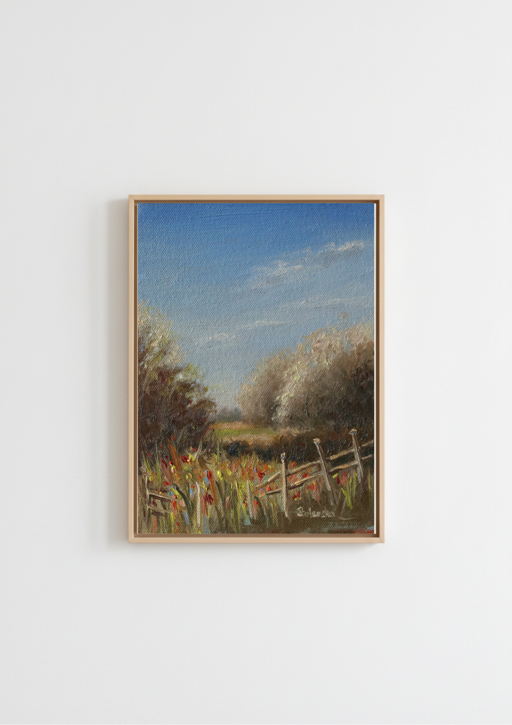 A framed landscape painting featuring a rustic fence, wildflowers, trees, and a blue sky, displayed on a plain white wall. Painting of a rural landscape with a wooden fence, grass, and trees under a blue sky. Original oil painting of a path towards the meadows at Carlton Marshes Suffolk, dilapidated fence and open fields