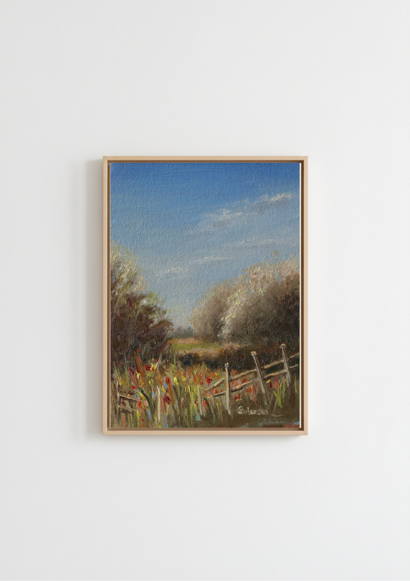 A framed landscape painting featuring a rustic fence, wildflowers, trees, and a blue sky, displayed on a plain white wall. Painting of a rural landscape with a wooden fence, grass, and trees under a blue sky. Original oil painting of a path towards the meadows at Carlton Marshes Suffolk, dilapidated fence and open fields