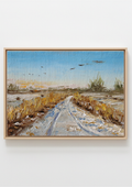 A framed landscape painting depicting a snowy path through a marshy field under a blue sky, mounted on a light gray wall. Painting of a rural landscape with a path, fields, and birds in the sky by a local artist. Original oil painting of geese in flight over snowy Oulton Broad marshes, snow-covered bridleway leading into scene