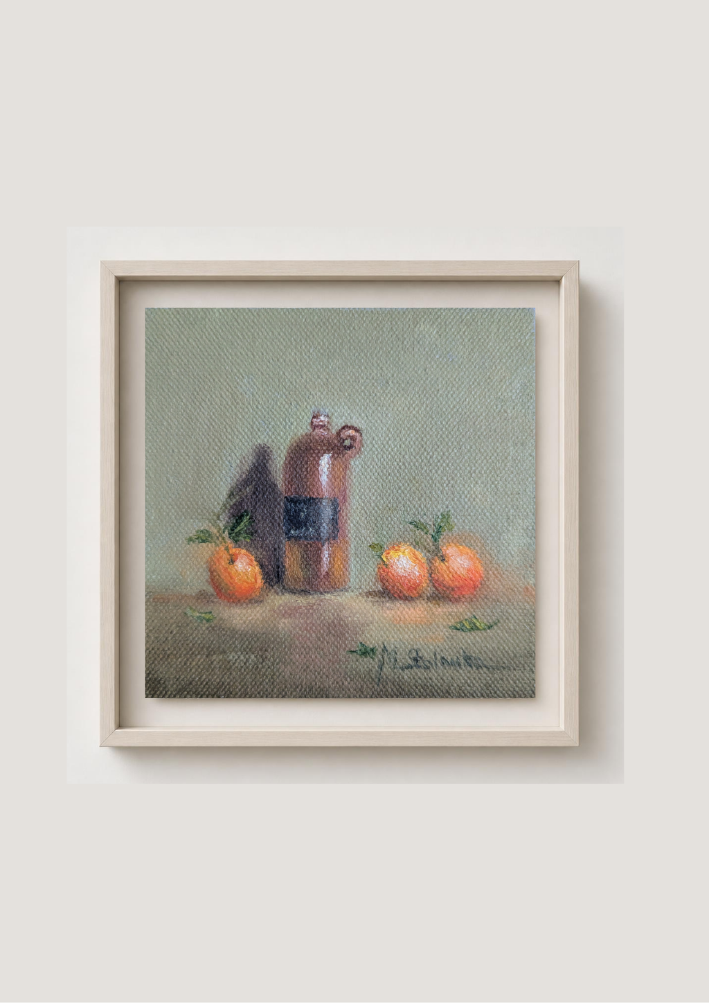 A framed still life painting featuring a brown bottle with a dark label and three small orange fruits on a textured green-gray background, presented in a light wood frame against a neutral beige wall. Original oil painting of a vintage bottle from Riga, antique glass vessel in a warm still life