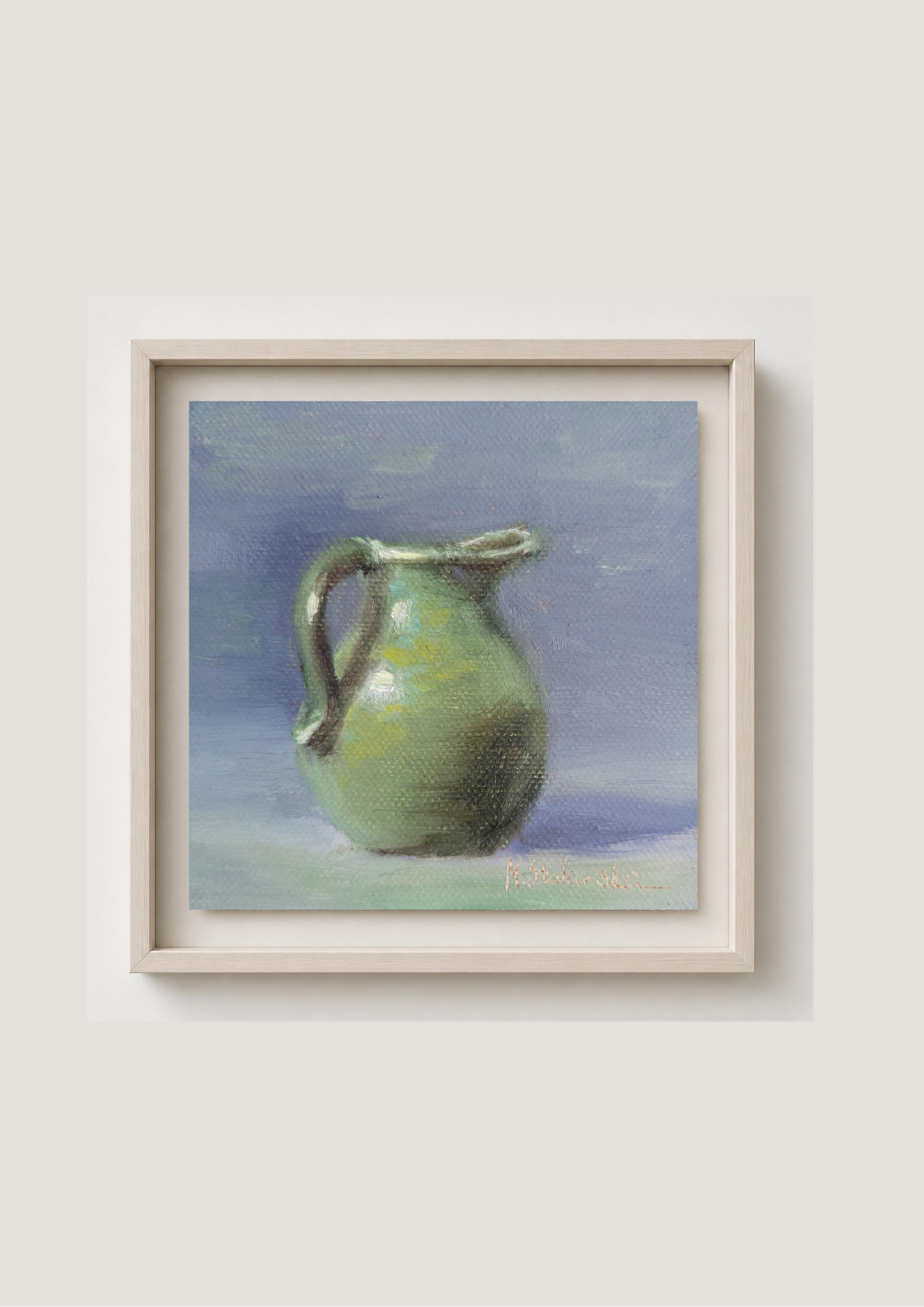 A framed still life painting of a green ceramic pitcher against a soft blue and purple background, mounted on a light beige wall.