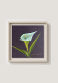 A framed painting of a white calla lily with green leaves on a dark purple background, set in a light beige frame against a neutral light gray wall.