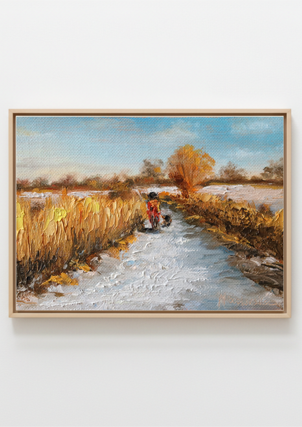 A framed landscape painting depicting a snowy path leading through golden fields toward a tree, with a small figure in red near the center, shown against a plain light gray background. Painting of a rural scene with a person on a bike and a dog, surrounded by fields and trees by a local artist. Original oil painting of a winter walk at Suffolk marshes, snow-covered landscape with figures