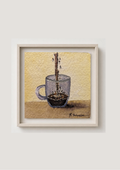 A framed watercolor painting of a glass mug with a coffee dripping in it, set against a textured cream background. The artwork is housed in a light-colored wooden frame and is displayed on a neutral light gray wall.